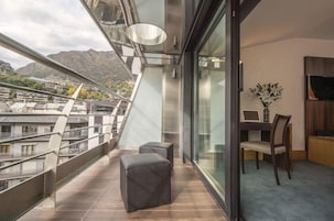 Un balcón moderno con vistas a la ciudad, zona de comedor con mesa y sillas, y un televisor montado.