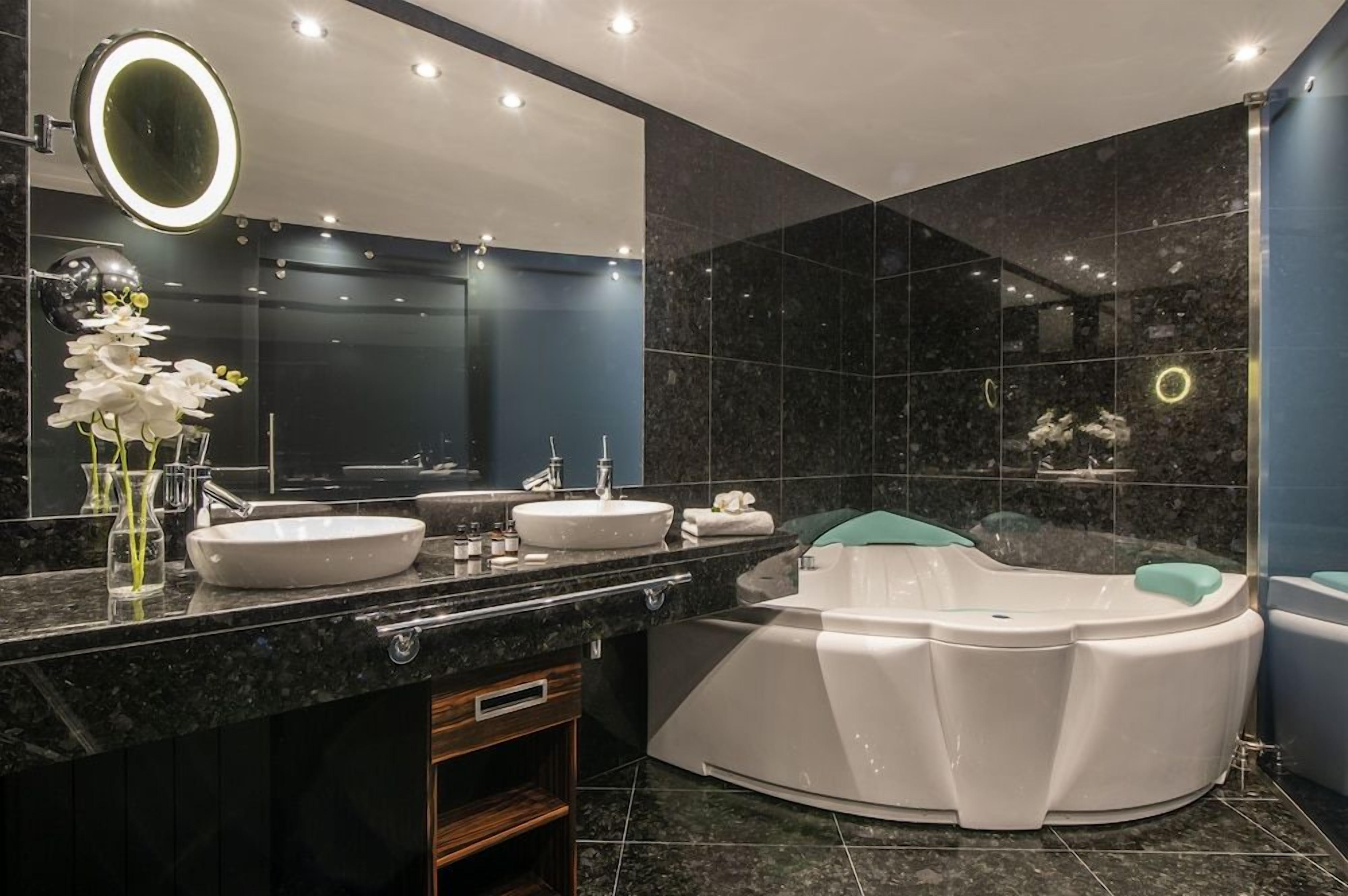Un baño moderno con un espejo grande, dos lavamanos, una bañera y un tocador con espejo.