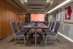Un salón de conferencias con una larga mesa, sillas y una pantalla que muestra un logotipo.