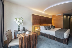 Una habitación de hotel con una cama, mesita de noche, una computadora portátil y un jarrón con flores.