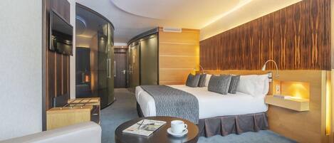 Una habitación de hotel moderna con cama, mesita de noche y zona de estar con mesa y sillas.