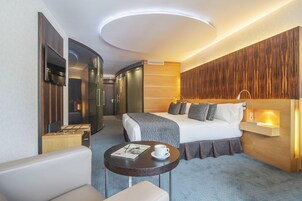 Una habitación de hotel moderna con cama, mesita de noche y zona de estar con mesa y sillas.