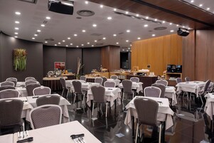 Un salón de conferencias con mesas, sillas, una zona de buffet y un escenario con proyector.