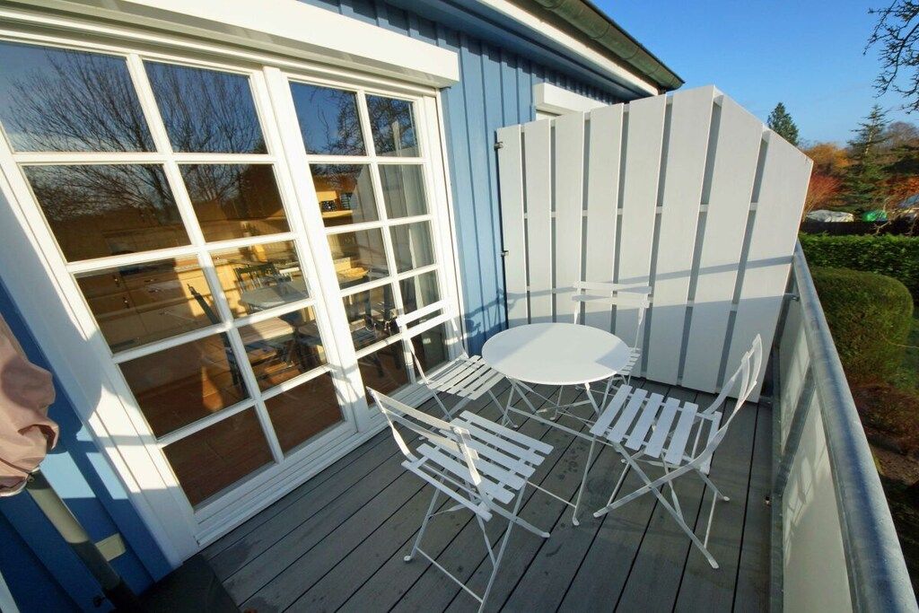 Una terraza con una mesa y sillas, cerca de una valla blanca y una ventana.
