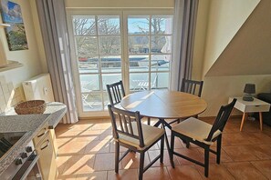 A kitchen with a round table and chairs, a radiator, and a window with curtains. - Holiday apartment with 2 bedrooms (Prerow)