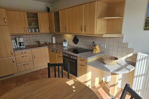 Une cuisine avec des meubles de rangement en bois, un plan de travail en granit, une cuisinière et une table à manger.