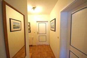 Un couloir avec des tableaux encadrés accrochés aux murs, une porte blanche dotée d’un panneau rectangulaire et un radiateur posé sur le sol.