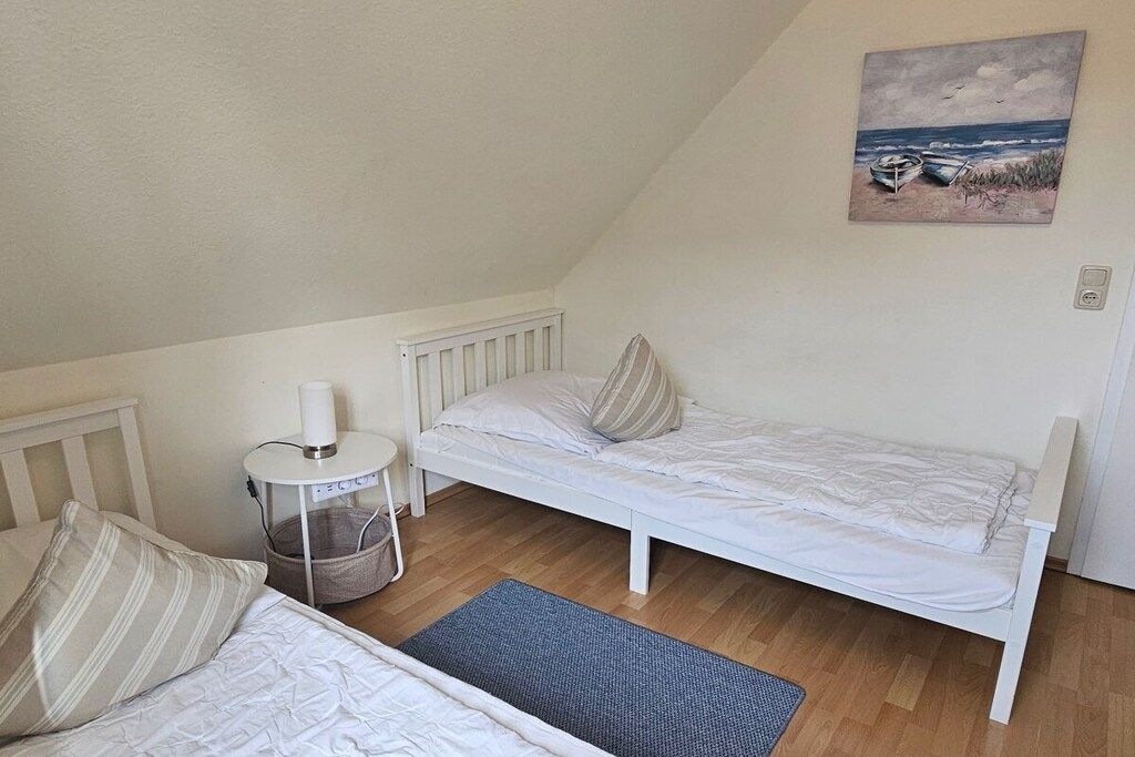 Ein Zimmer mit einem Einzelbett, einem weißen Kopfteil, einem Nachttisch mit Lampe und einem Bild einer Strandansicht an der Wand.