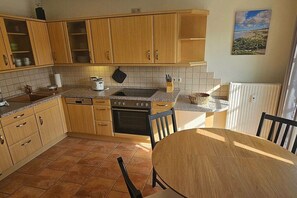 A kitchen with wooden cabinets, a stove, and a dining table with chairs. - Holiday apartment with 2 bedrooms (Prerow)