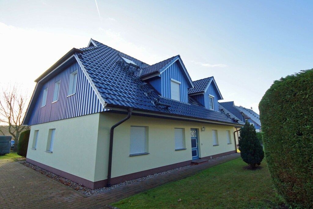 A two-story residential building with a sloped roof, a front entrance, and a small front yard.