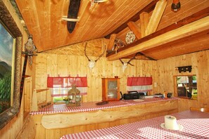 A wooden cabin interior with a dining area, a kitchen counter, and a window with red curtains. - at the Glöckner holiday farm (Muldenhammer OT Morgenröthe-Rautenkranz)