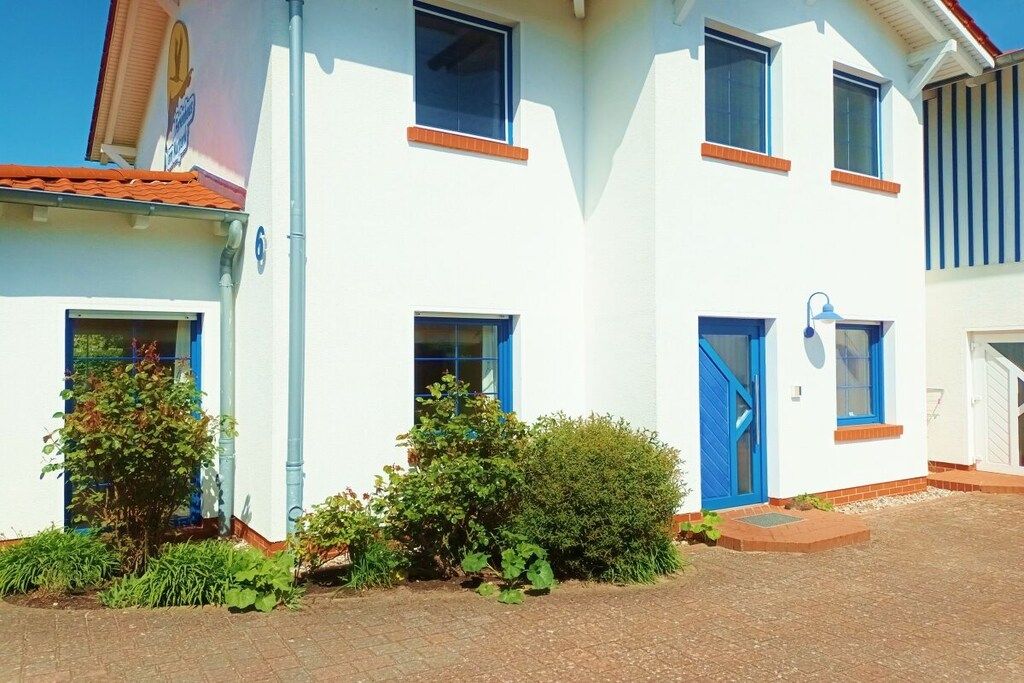 Ein zweistöckiges Gebäude mit weißer Fassade, blauen Fensterrahmen und einem roten Ziegeldach.