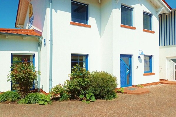 Un edificio a due piani con facciata bianca, finestre con cornici blu e tetto in tegole rosse.