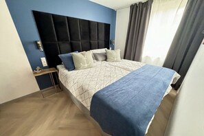 Ein Hotelzimmer mit Bett, Nachttisch, Wandlampe und einem Fenster mit Vorhängen.