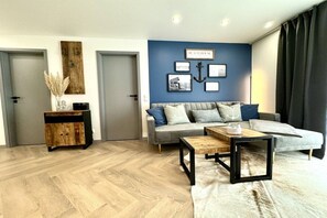 A modern living room with a grey sofa, wooden coffee table, and a decorative wall with framed pictures and an anchor. - Holiday apartment with 1 bedroom (Zingst)