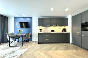 A modern kitchen with grey cabinets, a flat-screen TV mounted on the wall, and a dining area with a table and chairs. - Holiday apartment with 1 bedroom (Zingst)