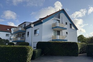 Ein zweistöckiges Wohngebäude mit einem Balkon im oberen Geschoss, einem roten Ziegeldach und einer gepflasterten Auffahrt.