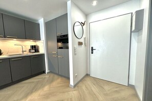 A modern kitchen with grey cabinets, a white door, and a wooden floor. - Holiday apartment with 1 bedroom (Zingst)