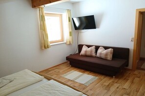 A room with a bed, a sofa, a television mounted on the wall, and a window with curtains. - Holiday apartment with 3 bedrooms (Rauris, AT-Österreich)