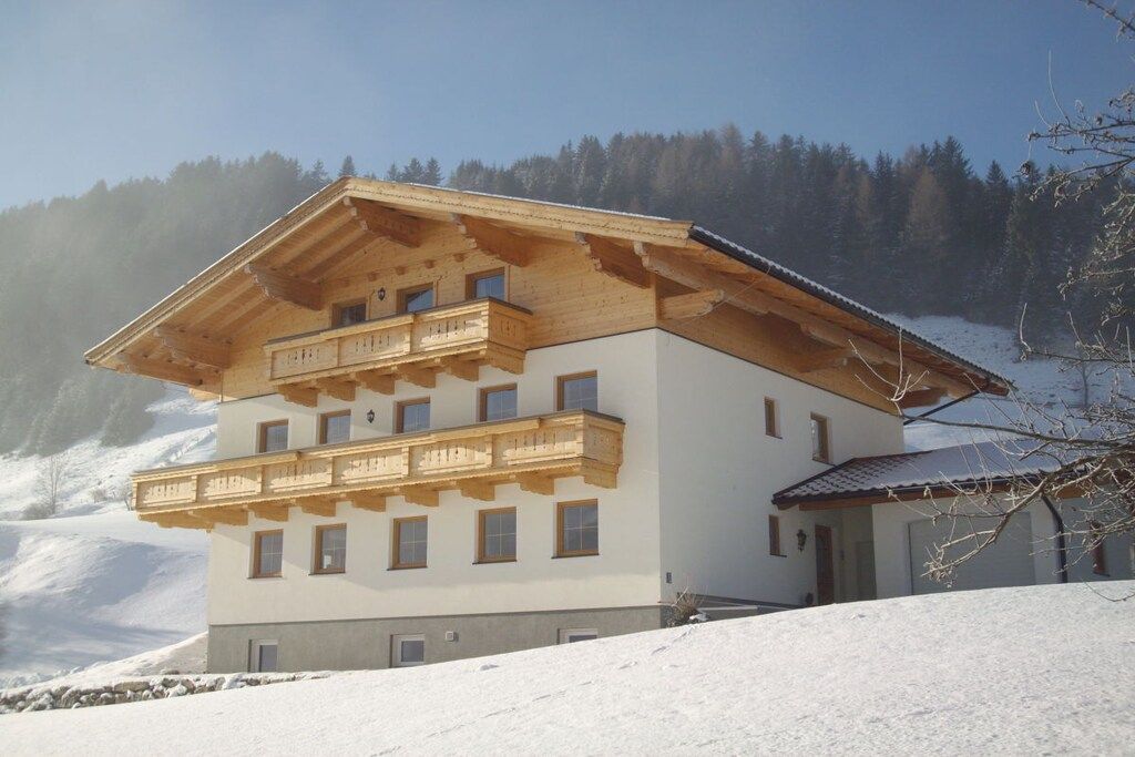 A multi-story wooden chalet with balconies, set against a snowy mountain backdrop.