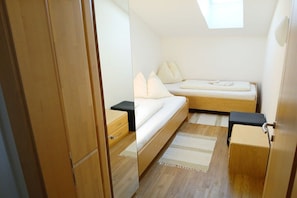 Ein Schlafzimmer mit einem Bett, Nachttischen, einem kleinen Hocker und einem Oberlicht.