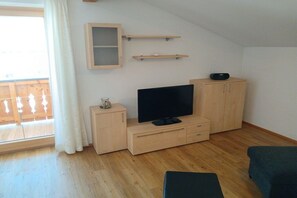 Ein Zimmer mit Fernseher auf einer Holzkommode, einem kleinen Tisch mit einer Dekoration und einer Glastür zum Außenbereich.