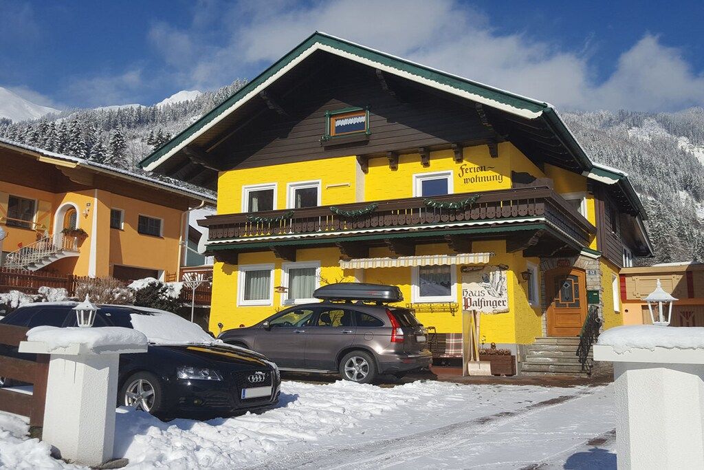 A yellow building with a balcony, a car parked in front, and snow-covered surroundings.