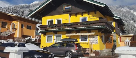 A yellow building with a balcony, a car parked in front, and snow-covered surroundings.