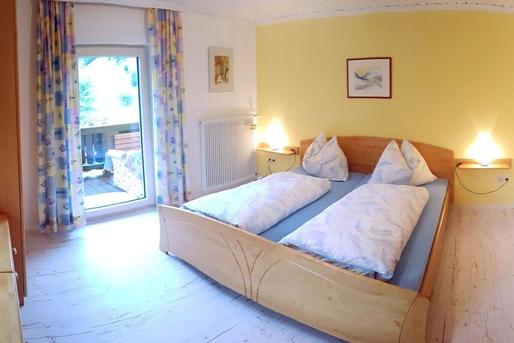 Een slaapkamer met een houten bed, twee bedlampen, een radiator en uitzicht door een glazen deur.