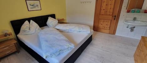 A bedroom with a bed, bedside table, wooden wardrobe, and a bathroom with a sink and mirror.