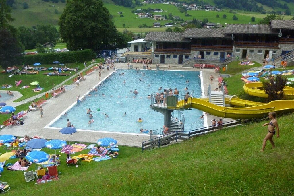 A swimming pool area with multiple pools, a lifeguard tower, and a building with a sloped roof.