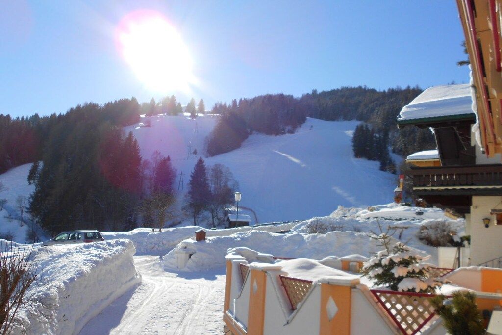 A snow-covered ski slope with a clear sky, a parked vehicle, and a building with a sloped roof.