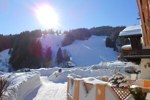 Une piste de ski enneigée, un ciel dégagé, un véhicule garé et un bâtiment doté d’un toit en pente.