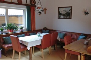 A dining area with a wooden table and benches, a window with curtains, and a painting on the wall. - Holiday apartment with 1 bedroom (Rauris)