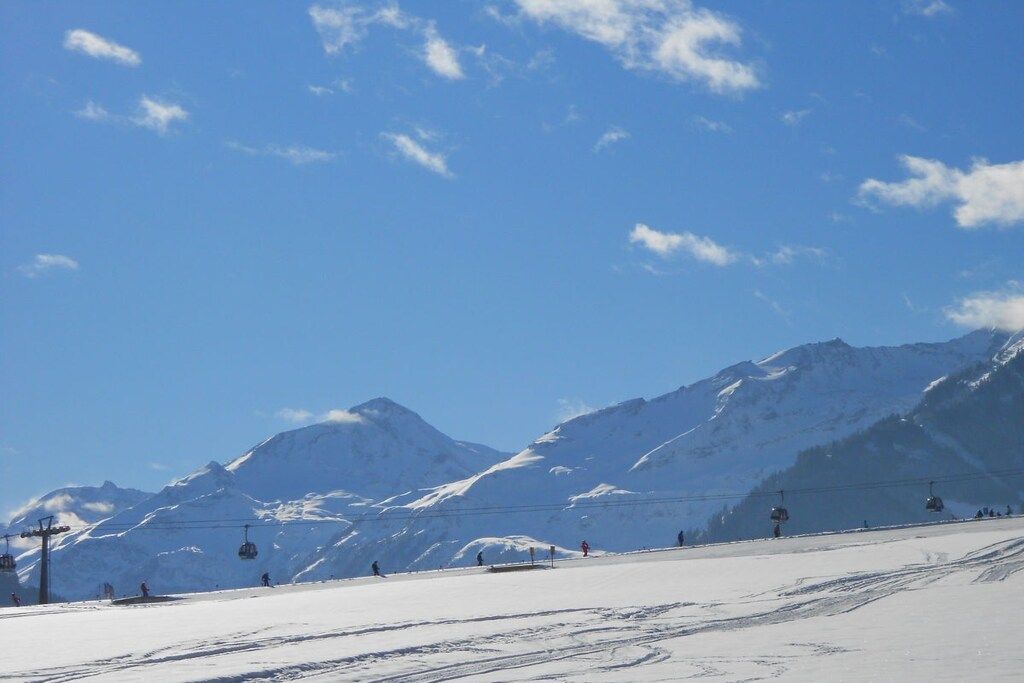 Ein mit Schnee bedeckter Ski-Hang mit Skiliften und Bergen im Hintergrund.