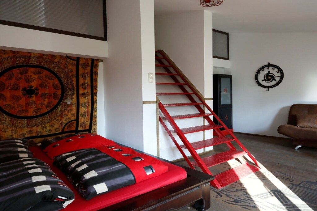 A room with a bed, a red ladder, a brown chair, and a tapestry on the wall.