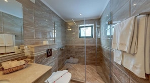 A modern bathroom with a glass-enclosed shower, marble walls, and a vanity with toiletries. - Antik (Balchik)