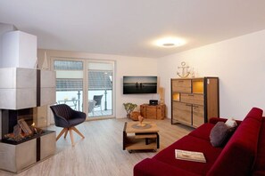 A modern living room with a fireplace, a red sofa, a television, and a wooden cabinet. - Holiday apartment with 3 bedrooms (Zinnowitz)