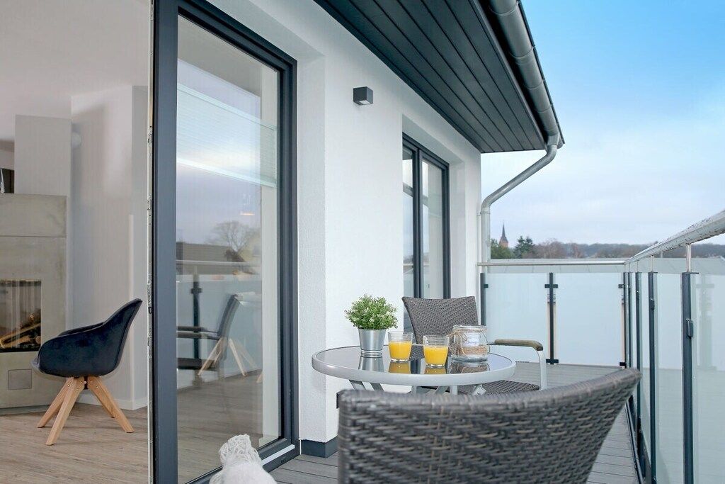 Ein moderner Balkon mit Glastrennwand, einem runden Tisch mit Stühlen und einem Blumentopf.