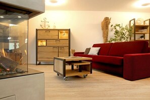 Een moderne woonkamer met een rode bank, een houten kast en een klein karretje.
