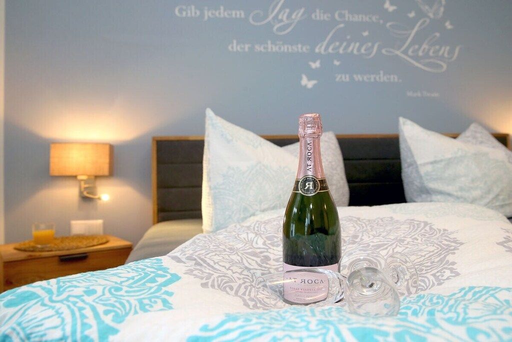 A bed with a bottle of champagne, a glass, and a decorative wall with a quote.