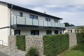 A modern two-story building with a balcony, stone wall, and well-maintained hedge. - Holiday apartment with 3 bedrooms (Zinnowitz)