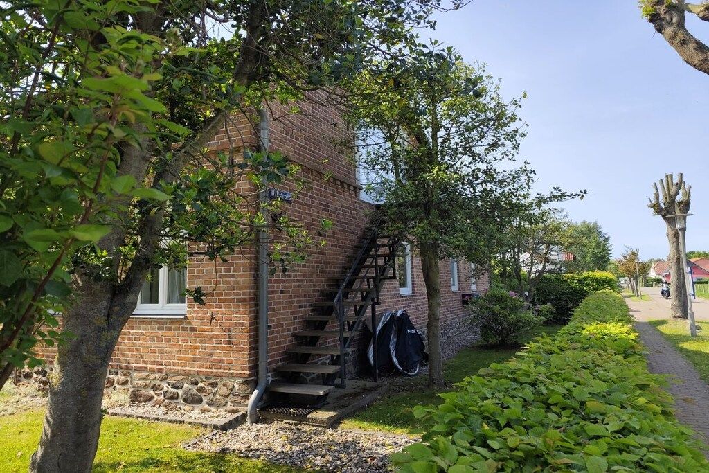 A brick building with a staircase leading to a window, surrounded by greenery and a clear sky.
