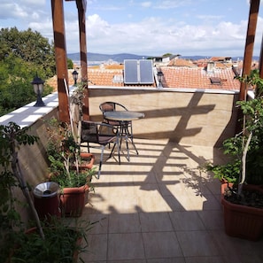 Terraza en la azotea con mesa y sillas, plantas en macetas y vistas de la ciudad.