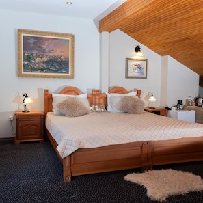 Un dormitorio con una cama grande, cabecera de madera, dos mesitas de noche con lámparas, un tocador y un cuadro en la pared, además de un escritorio pequeño con silla.