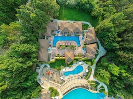 Vista aérea de um resort com várias piscinas, vegetação exuberante e diferentes edifícios.