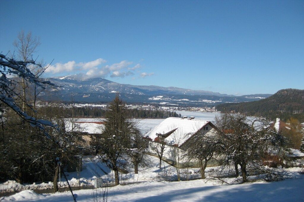 Een landelijk winterlandschap met besneeuwde huizen, een heldere lucht en op de achtergrond bergen.