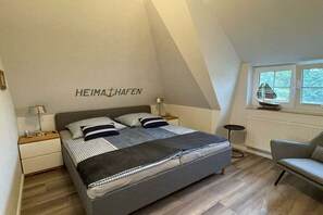 A bedroom with a bed, bedside tables, a chair, a window, and a wall with the name 'HEIMAHAFEN'. - Holiday home with 2 bedrooms (Seebad Karlshagen)