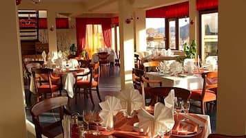 Un restaurante con varias mesas dispuestas para comer, que cuenta con una escalera y amplios ventanales con cortinas.