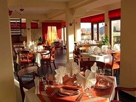 A restaurant with multiple tables set for dining, featuring a staircase and large windows with curtains.